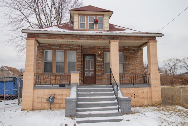 bungalow-style home featuring stone siding, fence, a porch, and brick siding