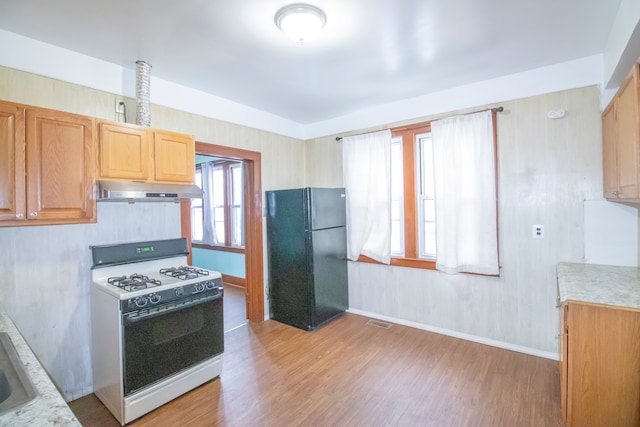 kitchen featuring white gas stove, light wood-style flooring, under cabinet range hood, light countertops, and freestanding refrigerator