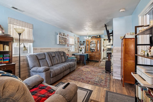 living room featuring a wainscoted wall, visible vents, an inviting chandelier, and wood finished floors