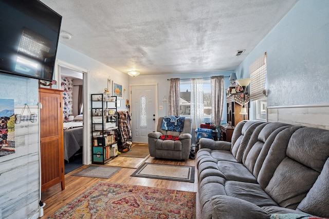 living area with light wood-style floors, visible vents, a textured ceiling, and a textured wall