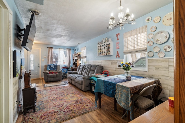 living room featuring a wainscoted wall, a notable chandelier, a textured ceiling, and wood finished floors