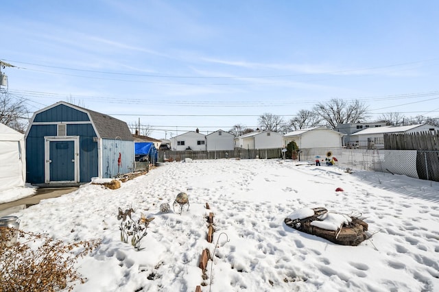 yard covered in snow featuring a shed, an outdoor structure, fence, and a residential view