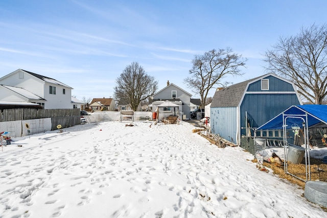 yard covered in snow with a storage shed, an outdoor structure, fence, and a residential view