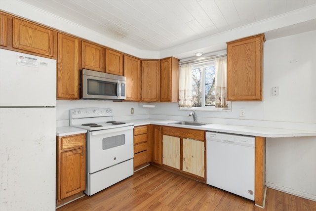 kitchen with white appliances, a sink, light countertops, brown cabinets, and light wood finished floors