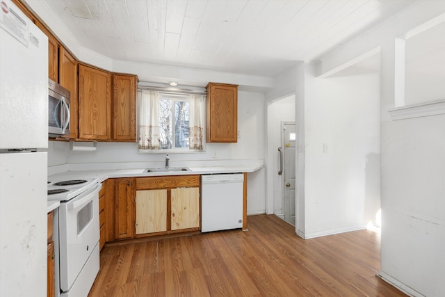 kitchen with white appliances, brown cabinetry, light countertops, light wood-type flooring, and a sink