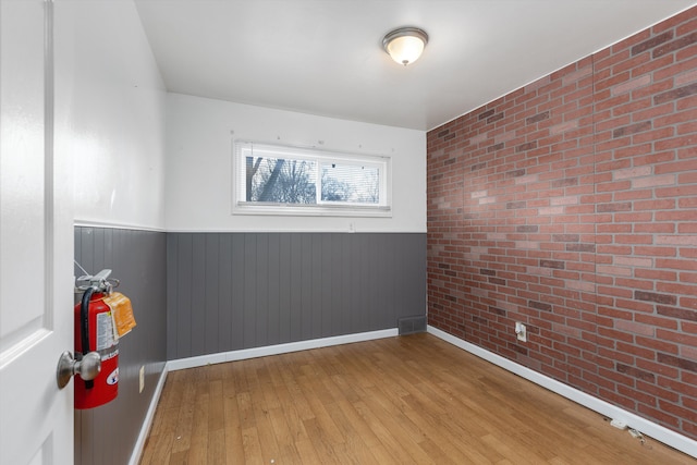 unfurnished room with visible vents, wainscoting, hardwood / wood-style floors, and brick wall