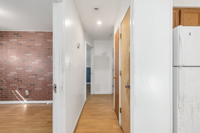 hall featuring baseboards, light wood finished floors, and brick wall