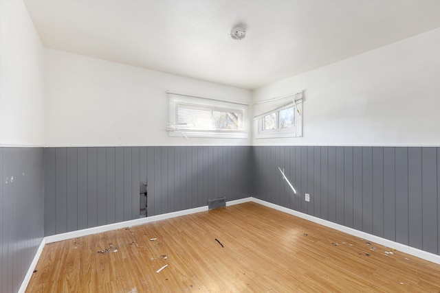 spare room with a wainscoted wall, baseboards, visible vents, and hardwood / wood-style floors