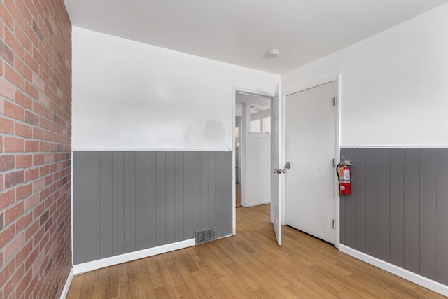 spare room with light wood-type flooring, wainscoting, visible vents, and brick wall