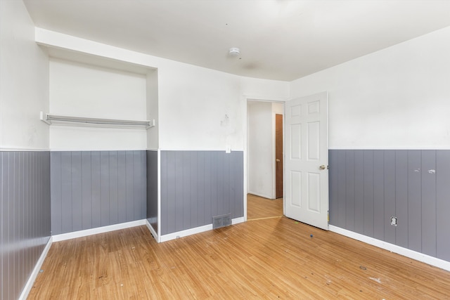 empty room featuring wooden walls, wainscoting, visible vents, and light wood finished floors