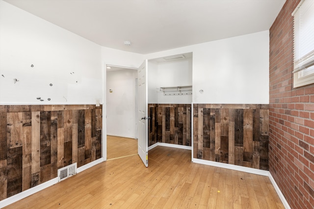 spare room featuring hardwood / wood-style flooring, brick wall, wood walls, visible vents, and wainscoting