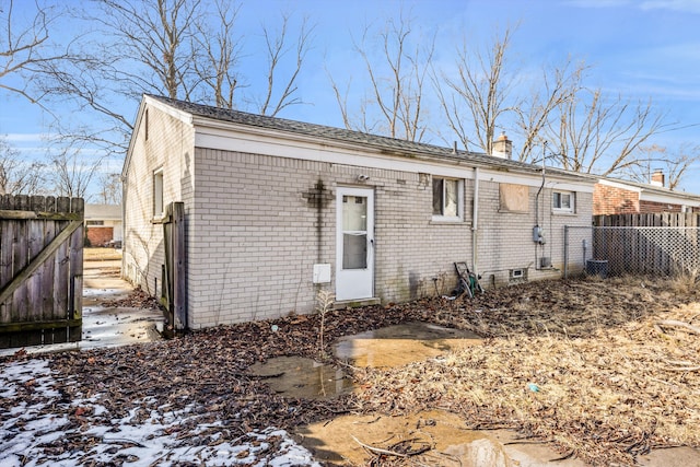 snow covered property with brick siding, fence, and a chimney