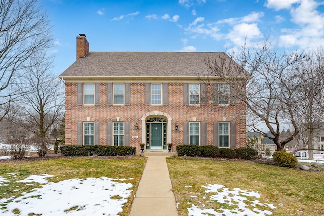 view of front of property featuring roof with shingles, brick siding, a chimney, and a lawn