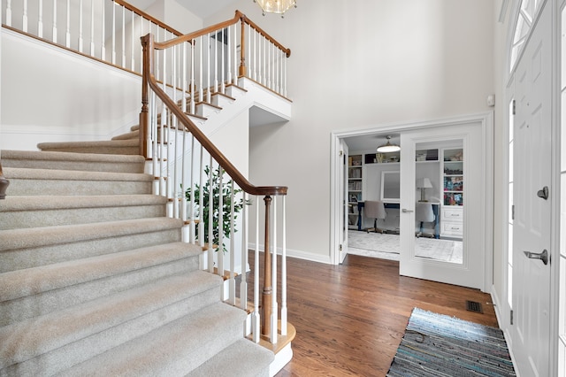 foyer featuring visible vents, baseboards, a towering ceiling, dark wood-style floors, and stairs