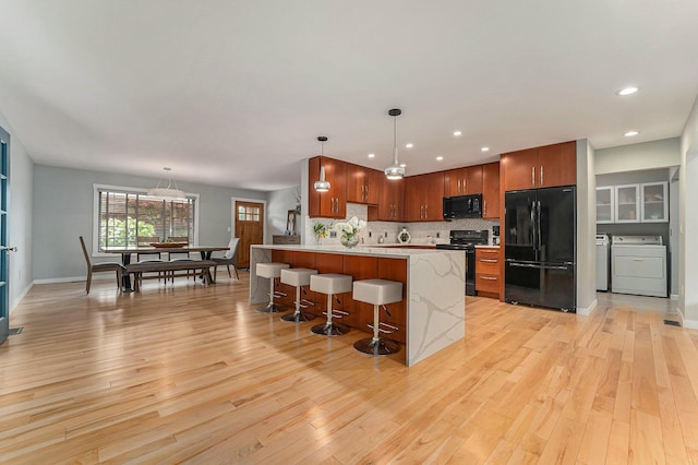 kitchen with a breakfast bar area, light wood-style floors, light countertops, black appliances, and pendant lighting