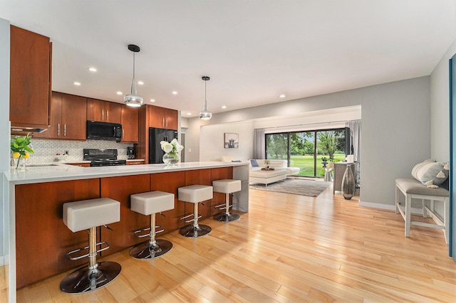 kitchen featuring a peninsula, light countertops, light wood-type flooring, black appliances, and decorative light fixtures