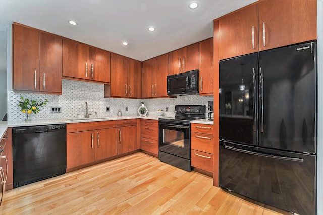 kitchen featuring light countertops, backsplash, a sink, light wood-type flooring, and black appliances