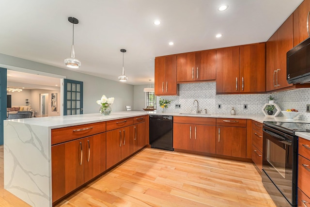 kitchen featuring a peninsula, a sink, light wood-type flooring, black appliances, and pendant lighting