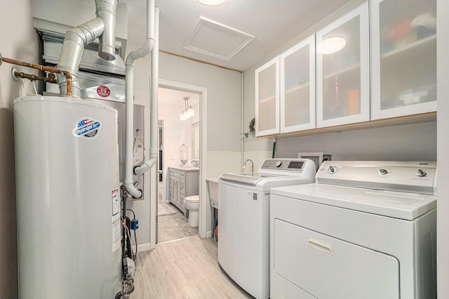 clothes washing area with gas water heater, light wood finished floors, cabinet space, attic access, and separate washer and dryer