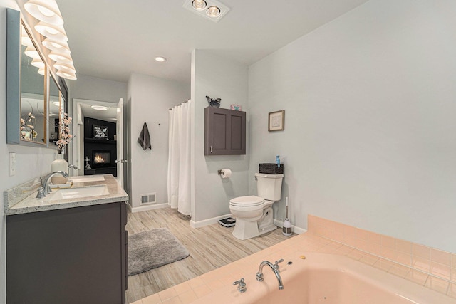 full bath featuring a fireplace, wood finished floors, vanity, visible vents, and a whirlpool tub