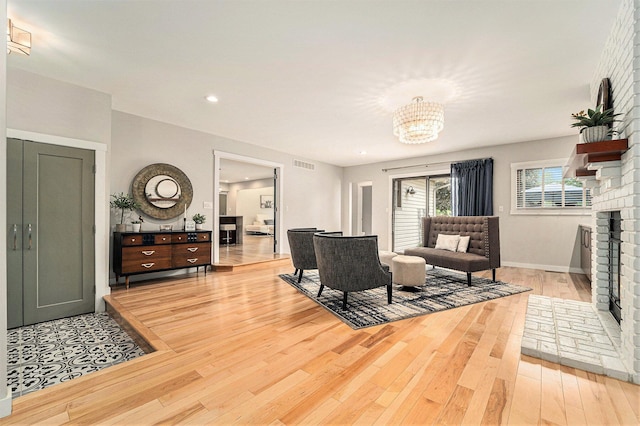 living room with baseboards, visible vents, wood finished floors, a brick fireplace, and a chandelier