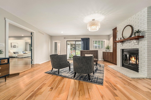 dining room with light wood-style flooring, a brick fireplace, visible vents, and an inviting chandelier