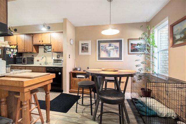 kitchen with baseboards, light countertops, light wood-type flooring, black appliances, and a sink