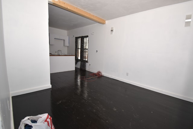 unfurnished room featuring dark wood-style floors, beam ceiling, and baseboards