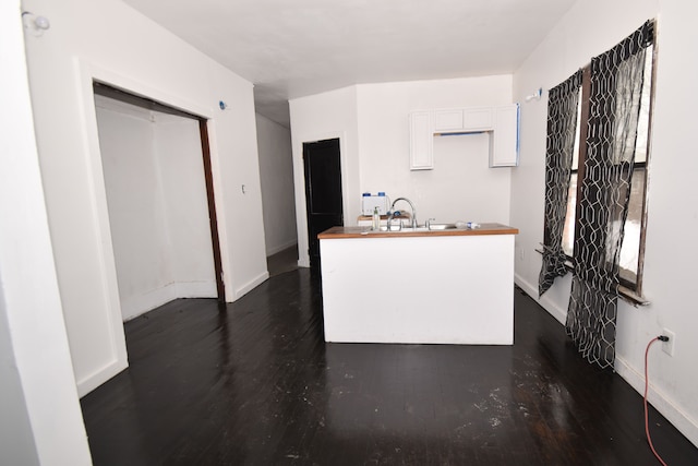 kitchen featuring butcher block countertops, white cabinetry, a sink, and baseboards