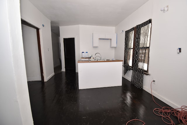 kitchen featuring butcher block countertops, a sink, baseboards, white cabinets, and dark wood-style floors