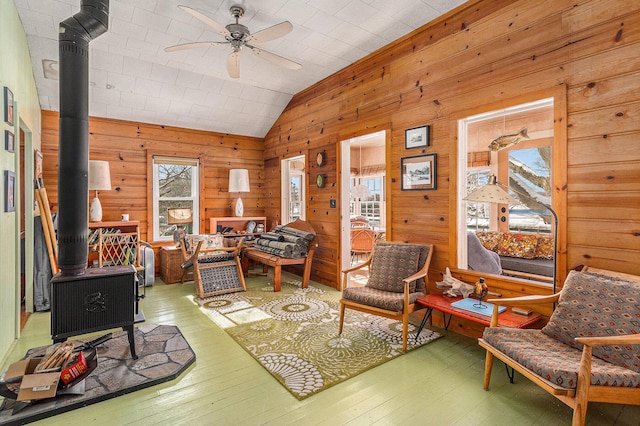 interior space with a wood stove, ceiling fan, wooden walls, and lofted ceiling