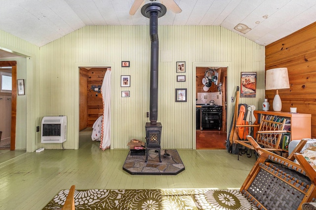 living room featuring heating unit, a wood stove, vaulted ceiling, and wood finished floors