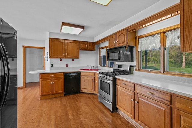 kitchen with black appliances, light wood-style floors, light countertops, and brown cabinets