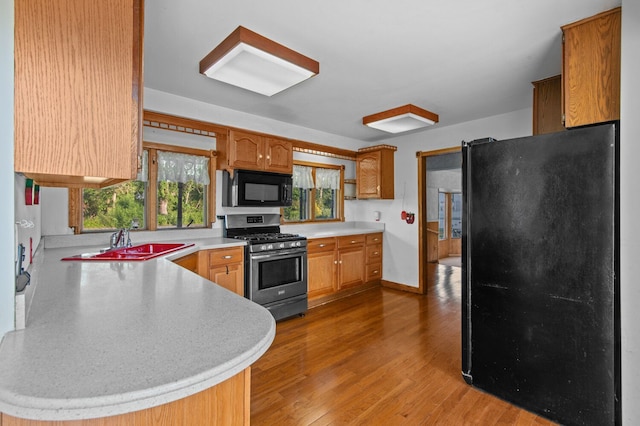 kitchen featuring a peninsula, black appliances, light wood-type flooring, and light countertops