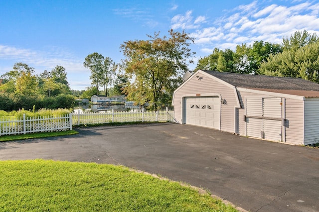 detached garage with driveway, a water view, and fence