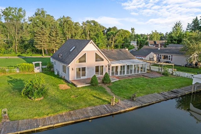 back of property with a sunroom, a water view, fence, and a lawn