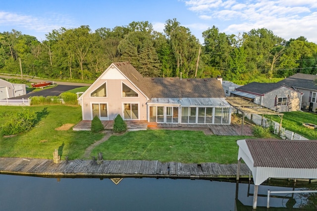 rear view of house with a water view, a sunroom, and a lawn