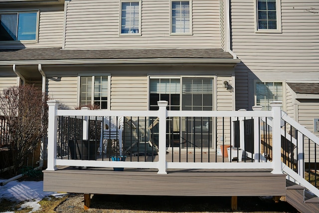 back of house featuring roof with shingles and a wooden deck