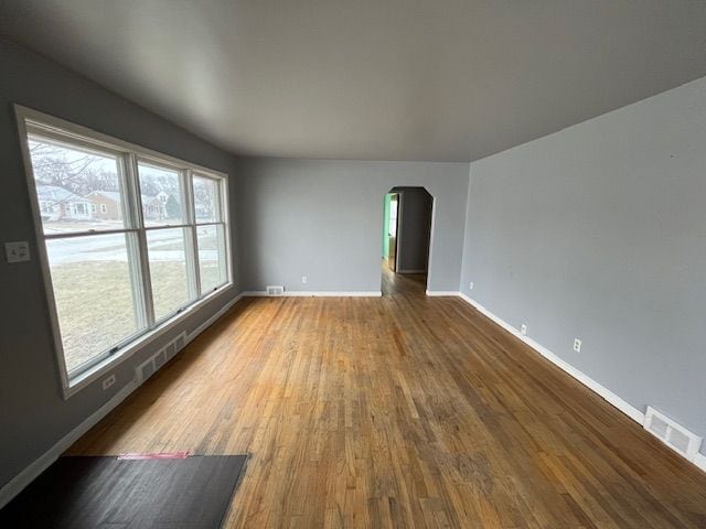 empty room featuring baseboards, visible vents, arched walkways, and wood finished floors