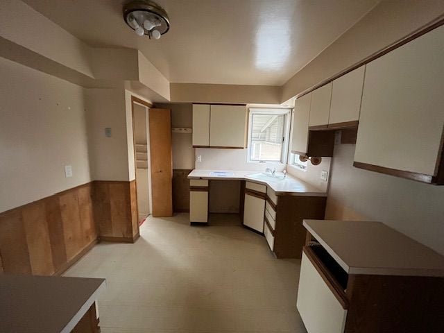 kitchen featuring a wainscoted wall, light countertops, wood walls, white cabinetry, and a sink