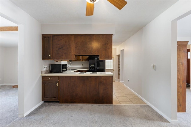 kitchen featuring light carpet, dark brown cabinetry, light countertops, and black fridge