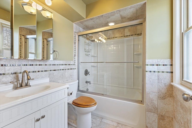 full bath with tile walls, toilet, wainscoting, combined bath / shower with glass door, and vanity