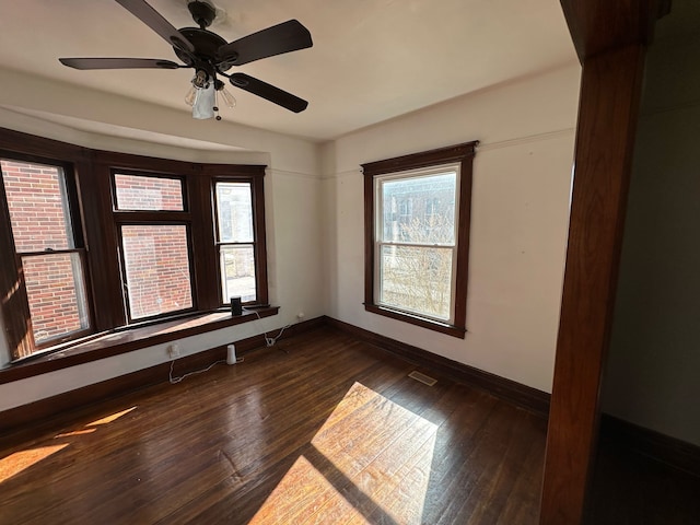 spare room featuring dark wood-style floors, visible vents, a healthy amount of sunlight, and baseboards