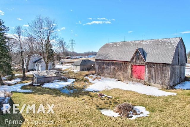 view of snow covered exterior featuring a barn, a garage, a lawn, and an outdoor structure