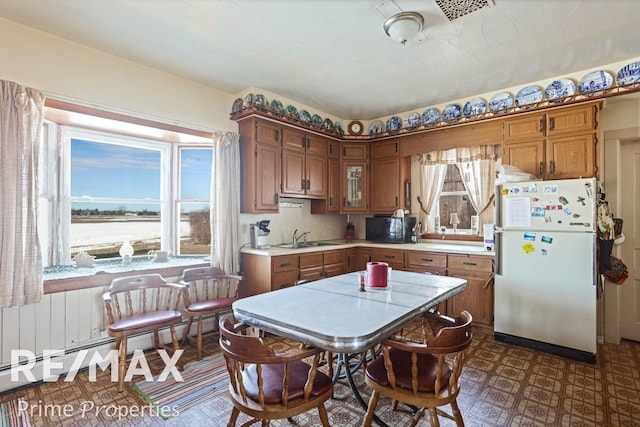 kitchen featuring dark floors, brown cabinets, light countertops, freestanding refrigerator, and a sink