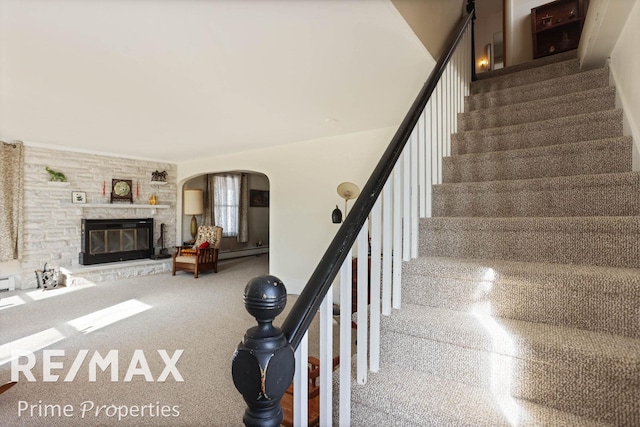 staircase with a baseboard radiator, a fireplace, and arched walkways