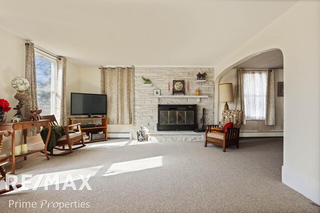 living area with carpet floors, a baseboard radiator, arched walkways, and a stone fireplace