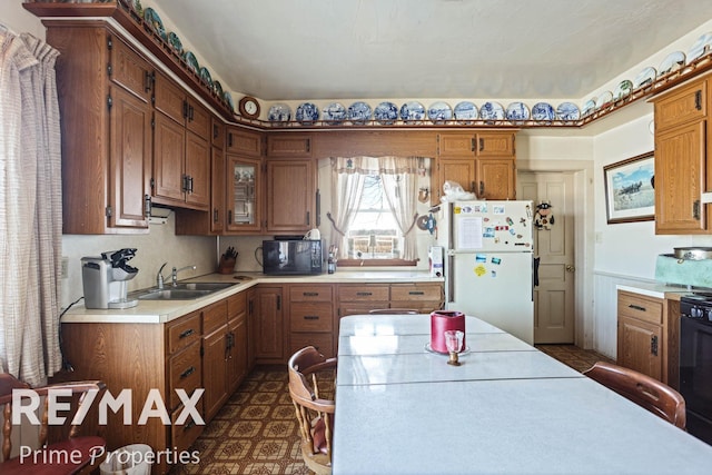 kitchen featuring brown cabinets, freestanding refrigerator, light countertops, black microwave, and a sink