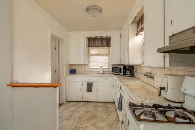 kitchen featuring under cabinet range hood, a sink, white cabinets, backsplash, and stainless steel microwave