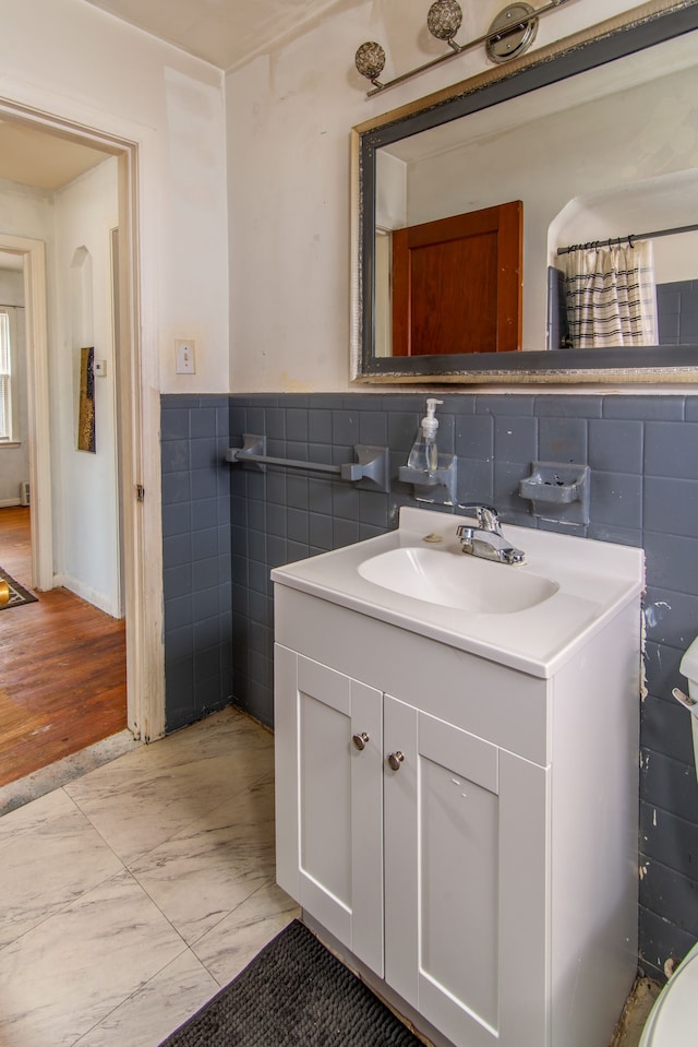 bathroom with marble finish floor, wainscoting, tile walls, and vanity